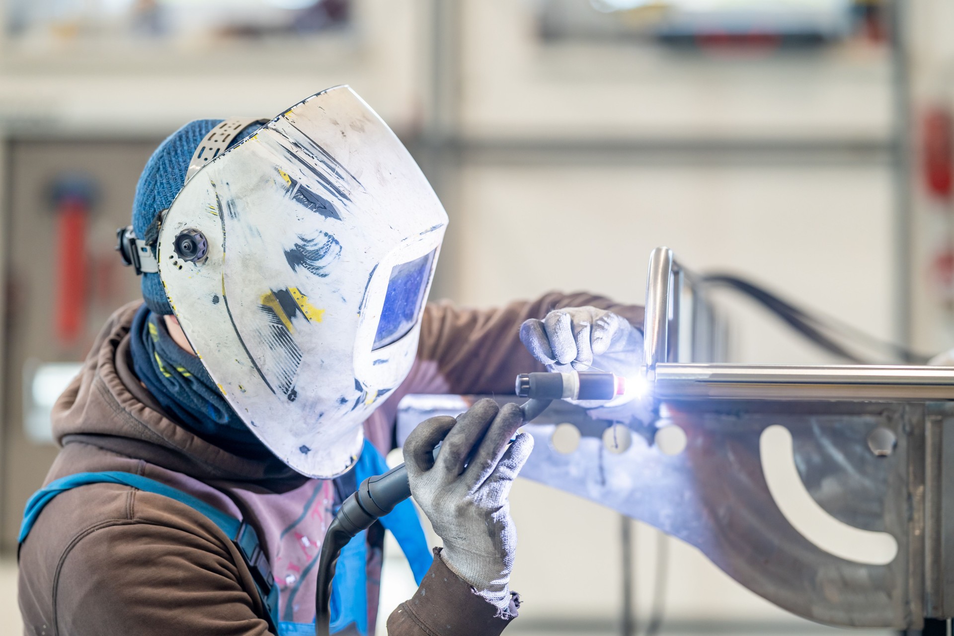 A man in personal protective equipment is welding metal in a factory