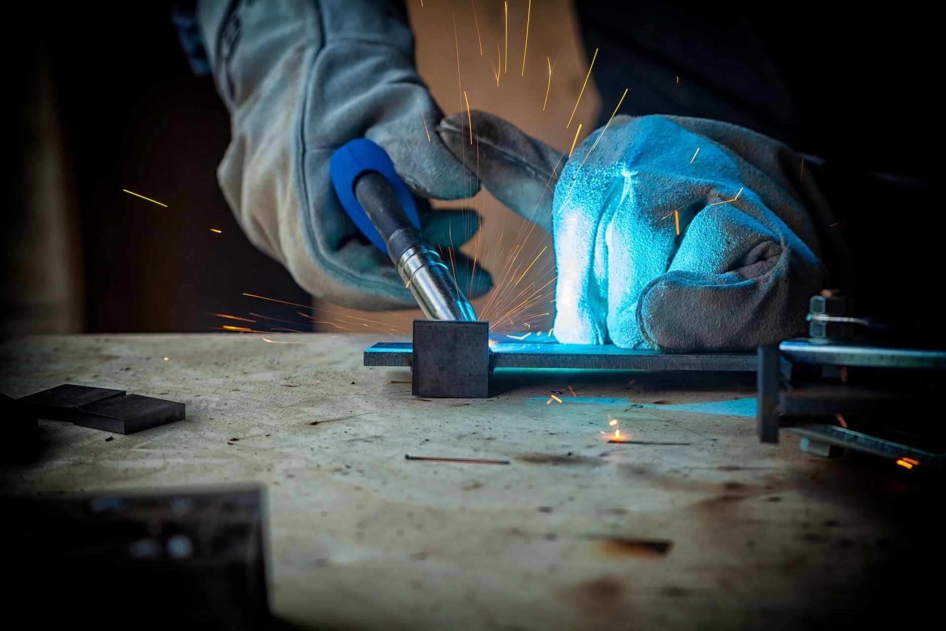 Strong man welder in work clothes hard working and welds with a welding machine metal 
 in the workshop